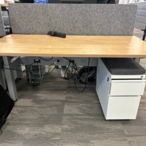 A used AMQ Kinex height-adjustable desk in a modern office setting, featuring a clean white worksurface, integrated power and data beam, and a privacy screen.