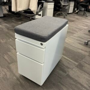 A used HAT Collective slim mobile filing pedestal in a modern office setting, featuring a compact 10.6-inch width, two drawers with a lock, and rolling casters for easy under-desk storage.