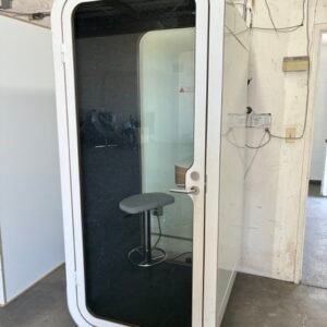 A used Framery O original soundproof office phone booth featuring a sleek, minimalist design with a glass door, built-in table, and an adjustable stool, providing a quiet space for private calls.