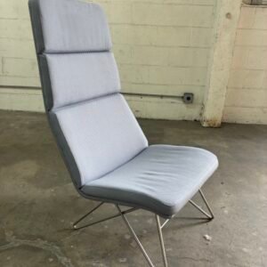 A used Source International CrissCross high back lounge chair featuring light blue-grey textured upholstery with horizontal channel stitching, supported by a distinctive chrome wire hairpin-style base.